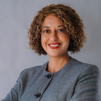A professional woman smiling confidently in a grey blazer against a neutral background.
